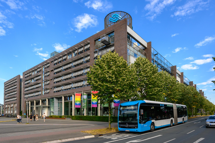 Ein Bürogebäude mit Regenbogen-Beflaggung und einem Elektrobus