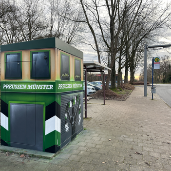 Eine Elektrobus-Ladestation steht am Straßenrand und ist mit SC Preußen Münster Grafiti besprüht.