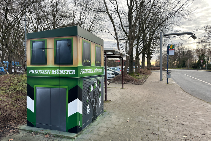 Eine Elektrobus-Ladestation steht am Straßenrand und ist mit SC Preußen Münster Grafiti besprüht.