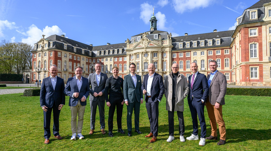 Kooperationspartner stehen vor dem Schloss in Münster. Die Sonne scheint.