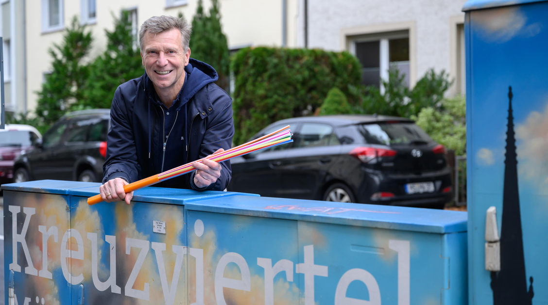 Mann hinter Verteilerkasten mit Glasfaserkabel in der Hand