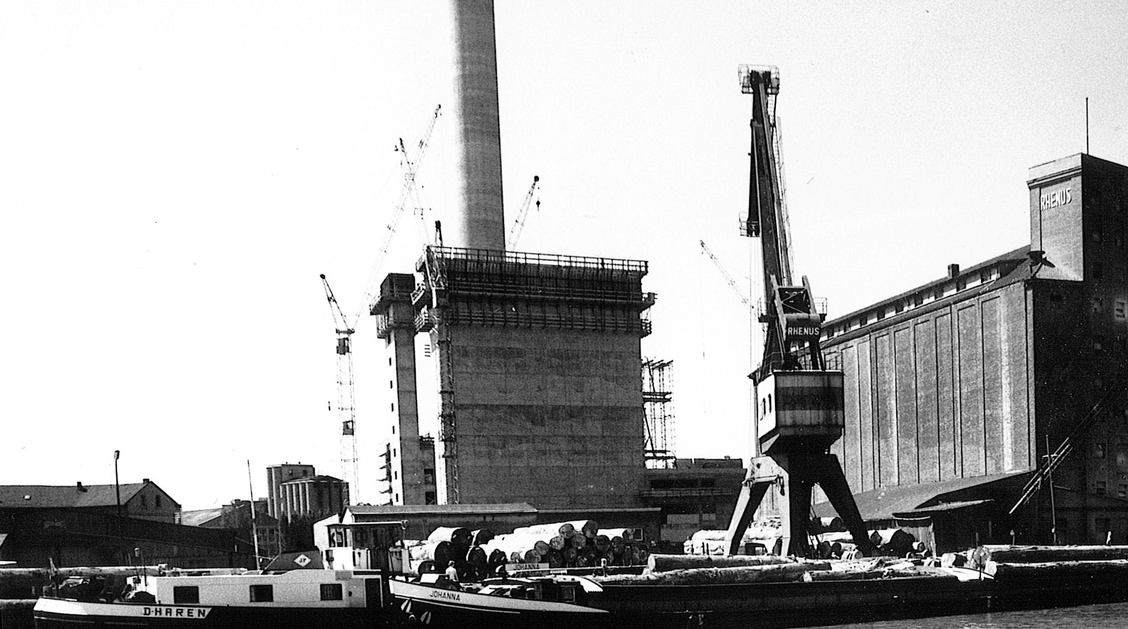 Ein Kraftwerk im Rohbau, davor liegen Schiffe in einem Hafen