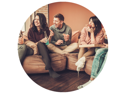 Eine Gruppe an jungen Leuten sitzt auf einem Sofa und isst Pizza.