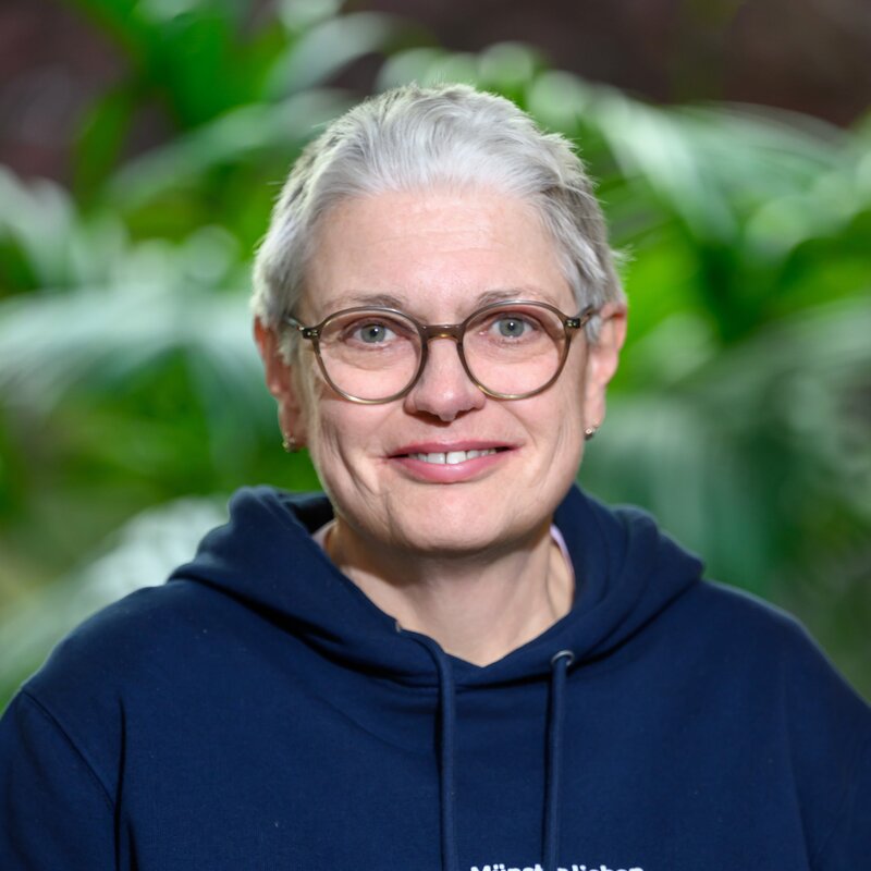 Christiane Puhe steht vor Büropflanzen und schaut freundlich in die Kamera.