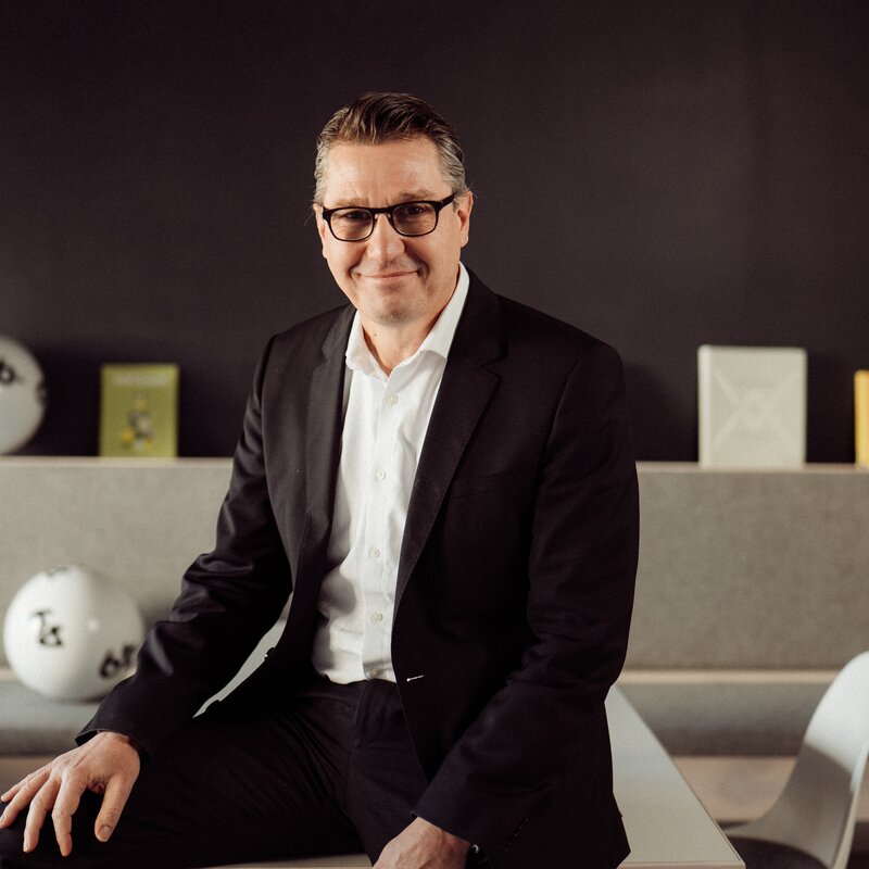 Ein Mann in weißen Hemd und schwarzen Anzug schaut freundlich in die Kamera.