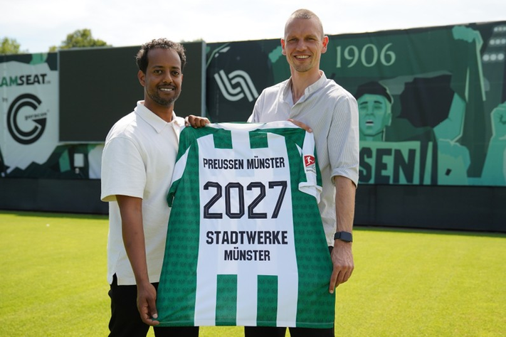 Nahom Estifanos und Ole Kittner stehen im Preußenstadion und halten ein Preußen-Trikot in den Händen.
