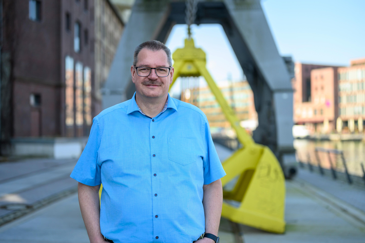 Ein Mann steht am Hafen und lächelt.