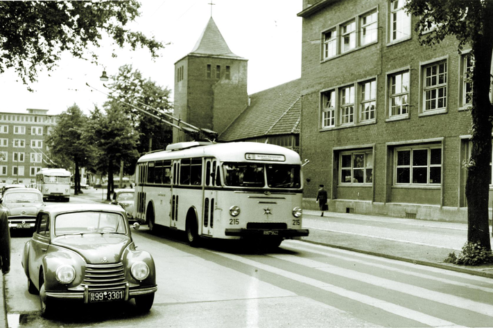 Ein Oberleitungsbus fährt über eine Straße, davor park ein Auto