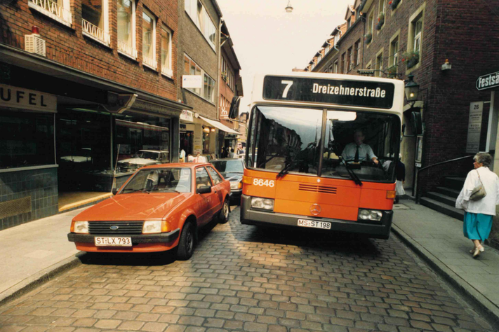 Ein Bus fährt durch eine enge Straße, links steht ein Auto