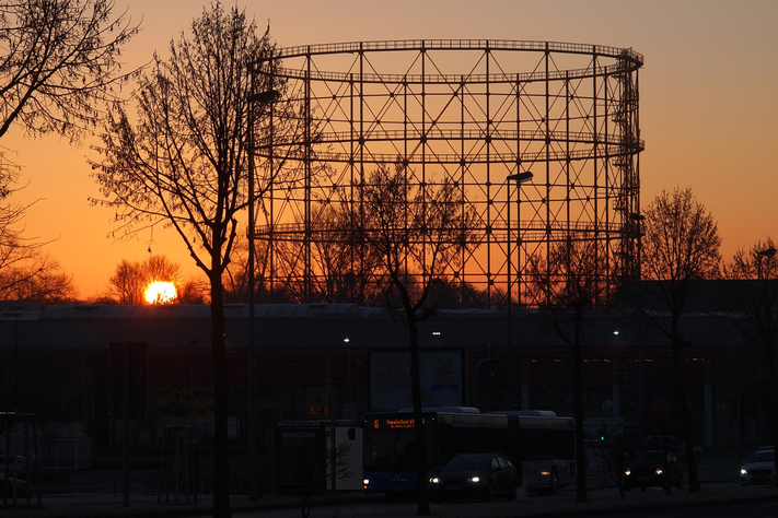 Das alte Gasometer ist im Gegenlicht zu sehen, die Sonne geht auf