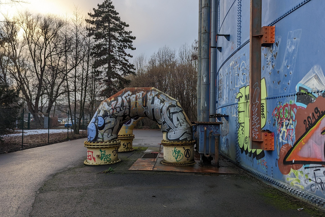 Zwei große Rohre, mit Graffiti besprüht, führen in ein Gebäude  