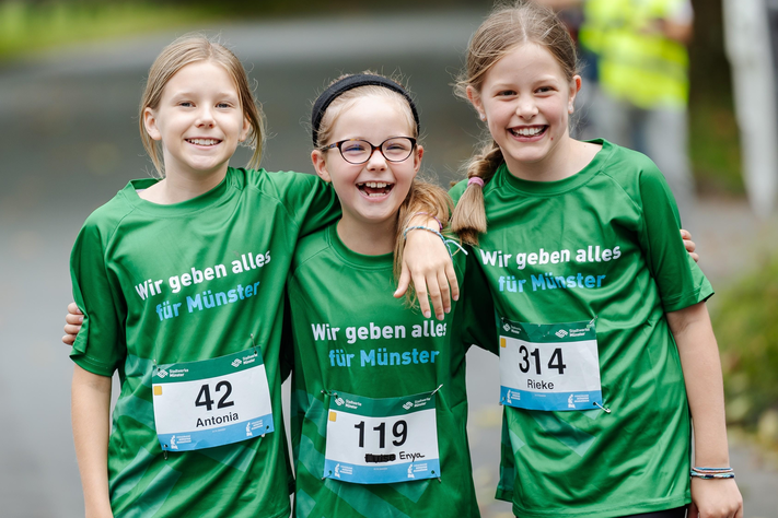 Drei junge Mädchen halten sich in den Armen und lachen.