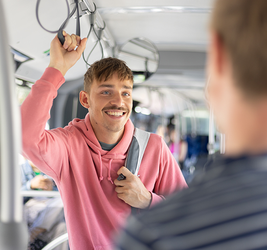 Junger Mann stehen im Bus und hält sich an einer Schlaufe fest.