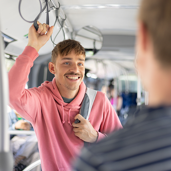 Junger Mann stehen im Bus und hält sich an einer Schlaufe fest.