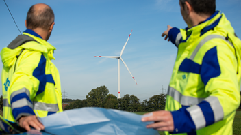 Zwei Stadtwerke Mitarbeiter und im Hintergrund ein Windrad zur Gewinnung von Windenergie.
