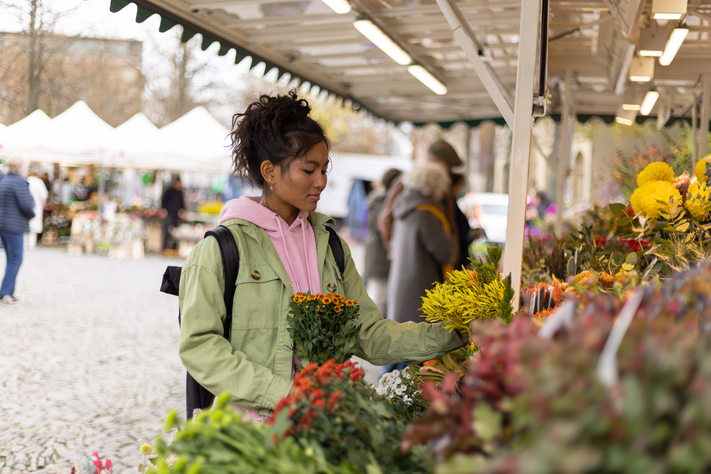Eine junge Frau betrachtet Blumen an einem Marktstand.