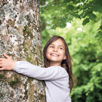 Kleines Mädchen umarmt den Stamm vom Baum.