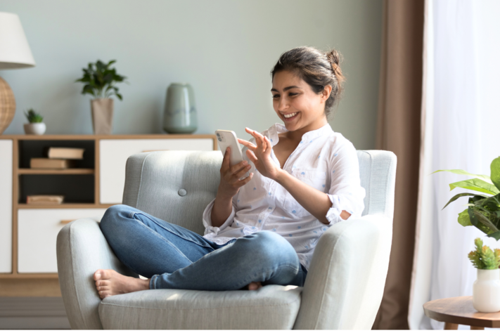 Junge Frau sitzt auf einem Sessel und schaut auf ihr Smartphone.