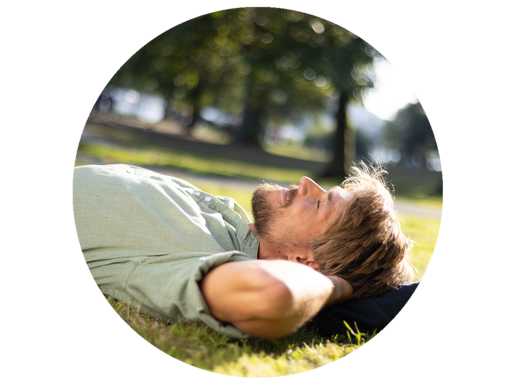 Ein Mann liegt entspannt im Gras in einem Park und genießt die Sonne.
