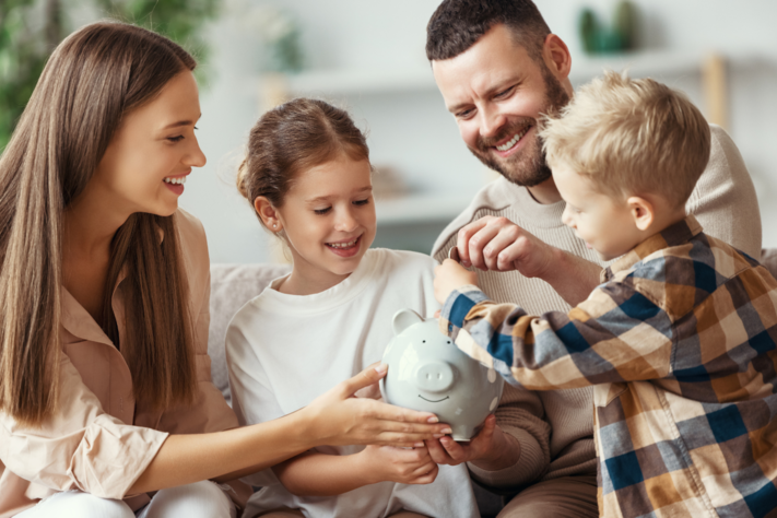 Eine junge Familie sitzt auf dem Sofa und betrachtet gemeinsam ihr Sparschwein.