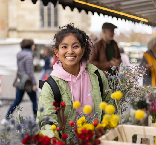 Eine junge Frau kauft auf dem Markt am Domplatz Blumen.
