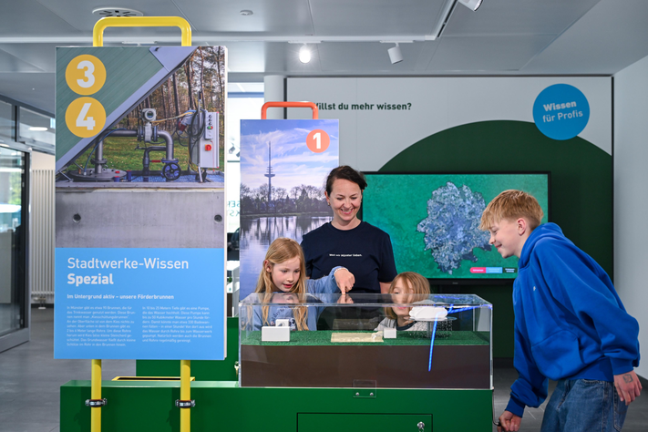 Drei kleine Kinder und eine Frau stehen an einem Wasserbecken in der Wasserwerkstatt.