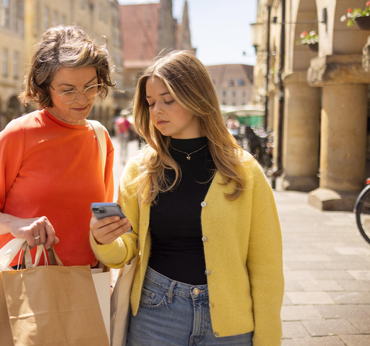 Eine junge Frau und ihre Mutter stehen auf dem Prinzipalmarkt und schauen auf ein Smartphone.