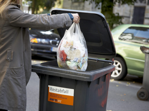 Müllsack wird in eine Mülltonne geworfen.