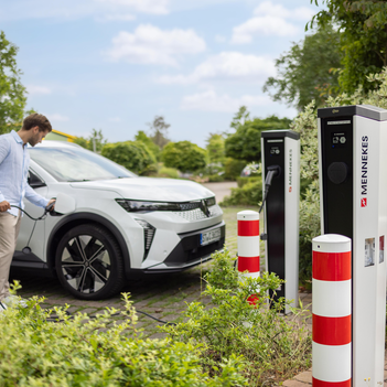 Ein Mann im Hemd tankt sein weißes E-Auto hinter zwei E-Ladesäulen von Mennekes.