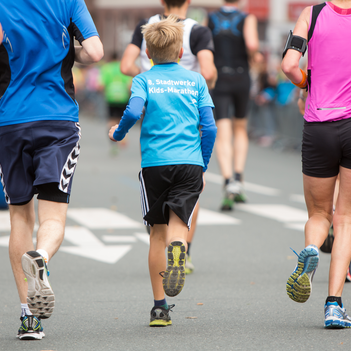 Kleiner Junge läuft mit zwei Erwachsenen beim Marathon.
