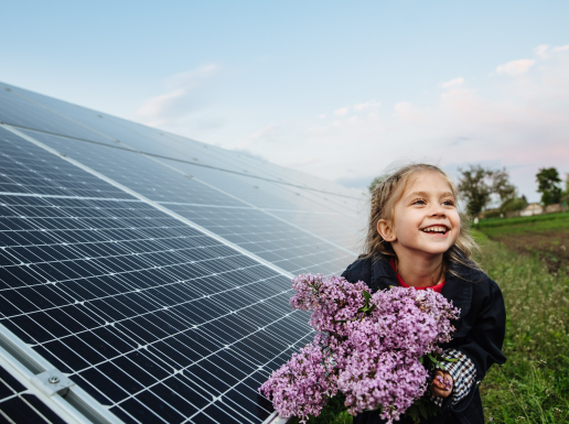 Kleines Mädchen mit Blumenstrauß in der Hand, im Hintergrund Photovoltaikmodule.