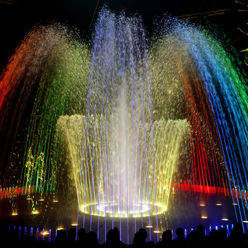 Ein Wasserspringbrunen wird mit buntem Licht angestrahlt.