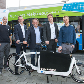 Fünf Männer stehen hinter einem Lastenrad, im Hintergrund steht ein Stadtbus.