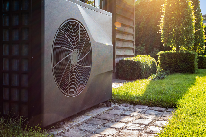 Eine Wärmepumpe neben einem Haus im sonnigen Garten.