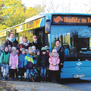 Kindergarten Gruppe steht vor einem Stadtbus.