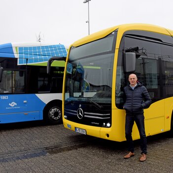Frank Gäfgen mit dem gelben Testbus vor zwei blauen Elektrobussen der Stadtwerke.