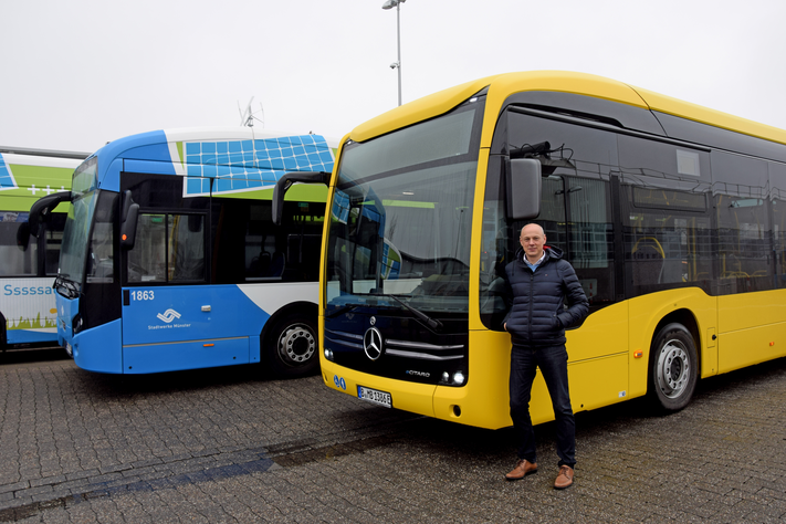 Frank Gäfgen mit dem gelben Testbus vor zwei blauen Elektrobussen der Stadtwerke.