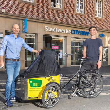 Zwei Männer stehen mit einem Lastenrad vor dem Stadtwerke Cityshop.