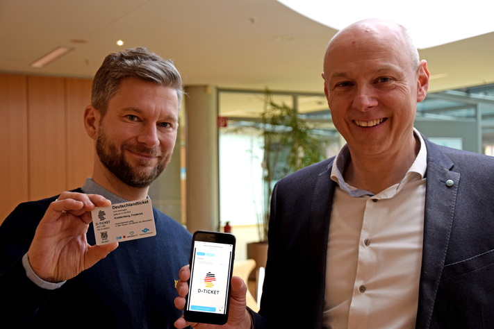 Frederick Koddenberg (l.) und Frank Gäfgen zeigen das Deutschlandticket, das es auf Chipkarte und als digitales Ticket in der App geben wird.