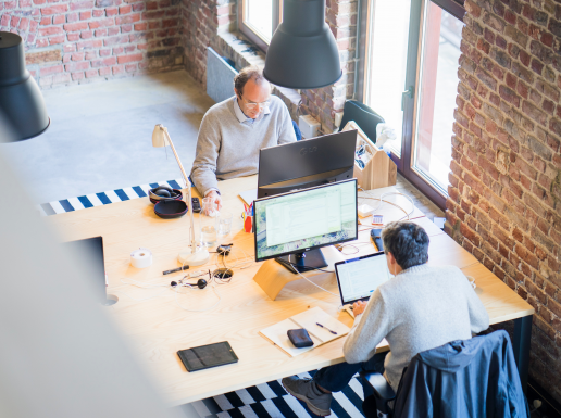 Zwei Männer sitzen an Schreibtischen und arbeiten an ihren Computern in einem Büro.