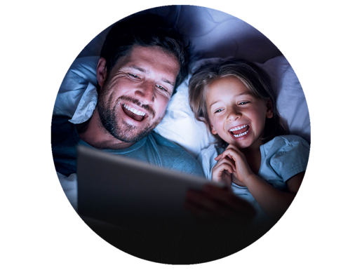 Vater und  kleine Tochter liegen im Bett und schauen auf ein Tablet.