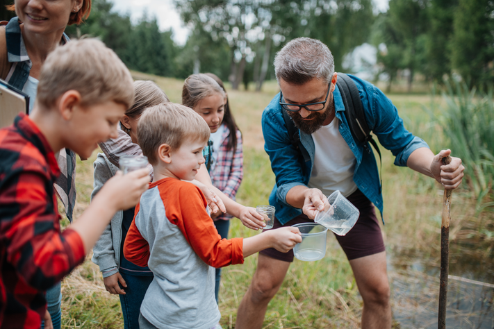 Ein Mann zeigt einer Gruppe von Kindern etwas in der Natur.